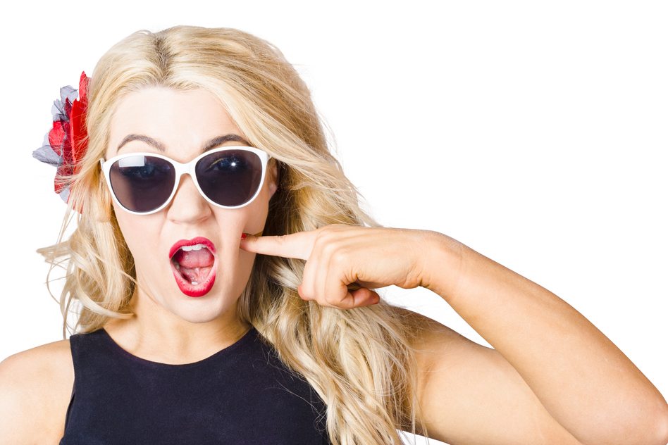 Crazy isolated portrait of a shocked blonde woman wearing sunglasses with pin-up makeup pressing cheek in a depiction of cosmetic application